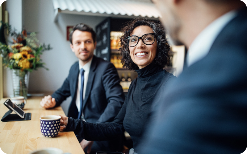 An image of a woman comfortably seated in an office, holding a mug in her hand, engaged in a discussion with her male colleagues.