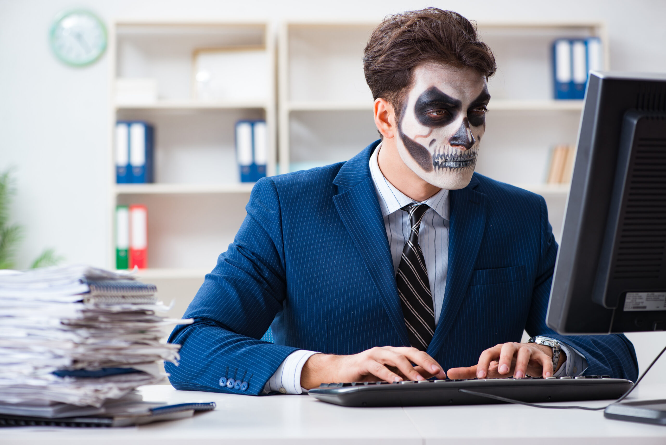 An accountant wearing Halloween attire, sitting at a desk adorned with spooky decorations, while focused on financial documents and calculations.